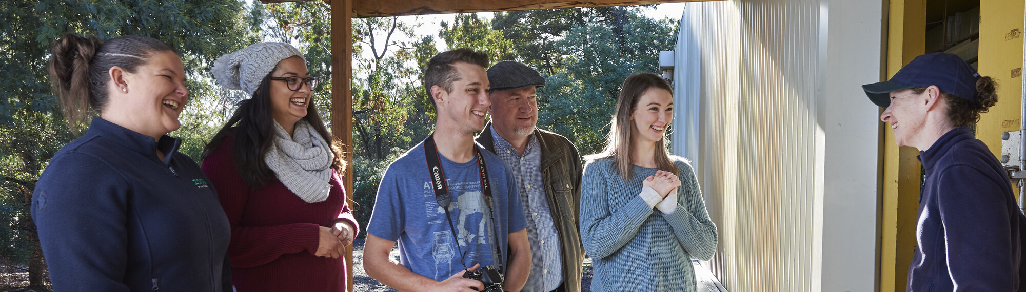 Two Zoo keepers stand with a group of four adults, all grinning.