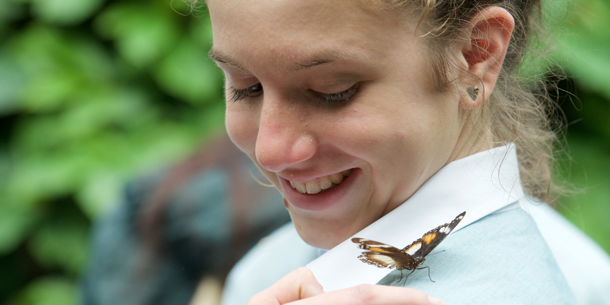 A secondary student smiles as she looks at a Monarch Butterfly on her left shoulder.