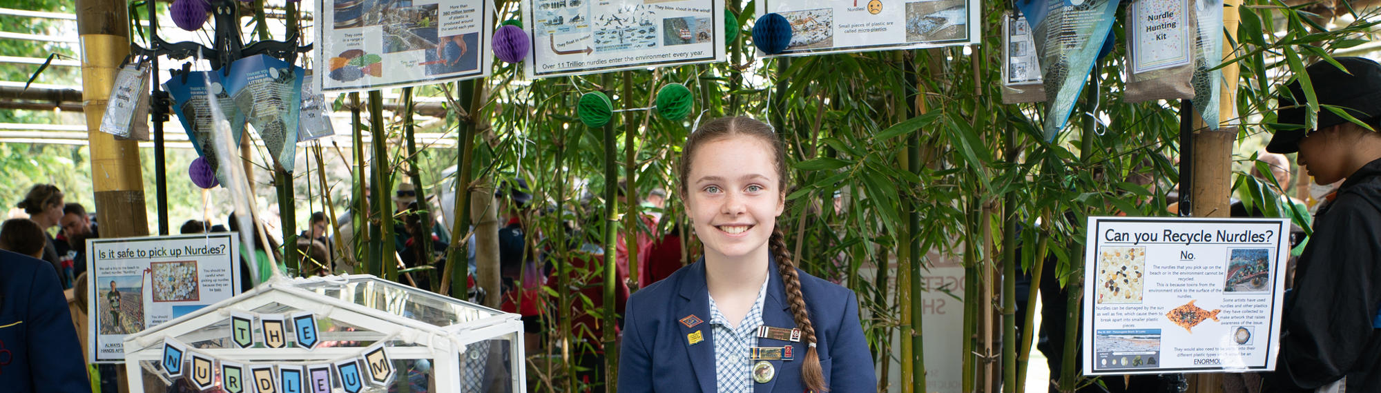 A school student stands smiling behind her craft Schools showcase, featuring nurdles.