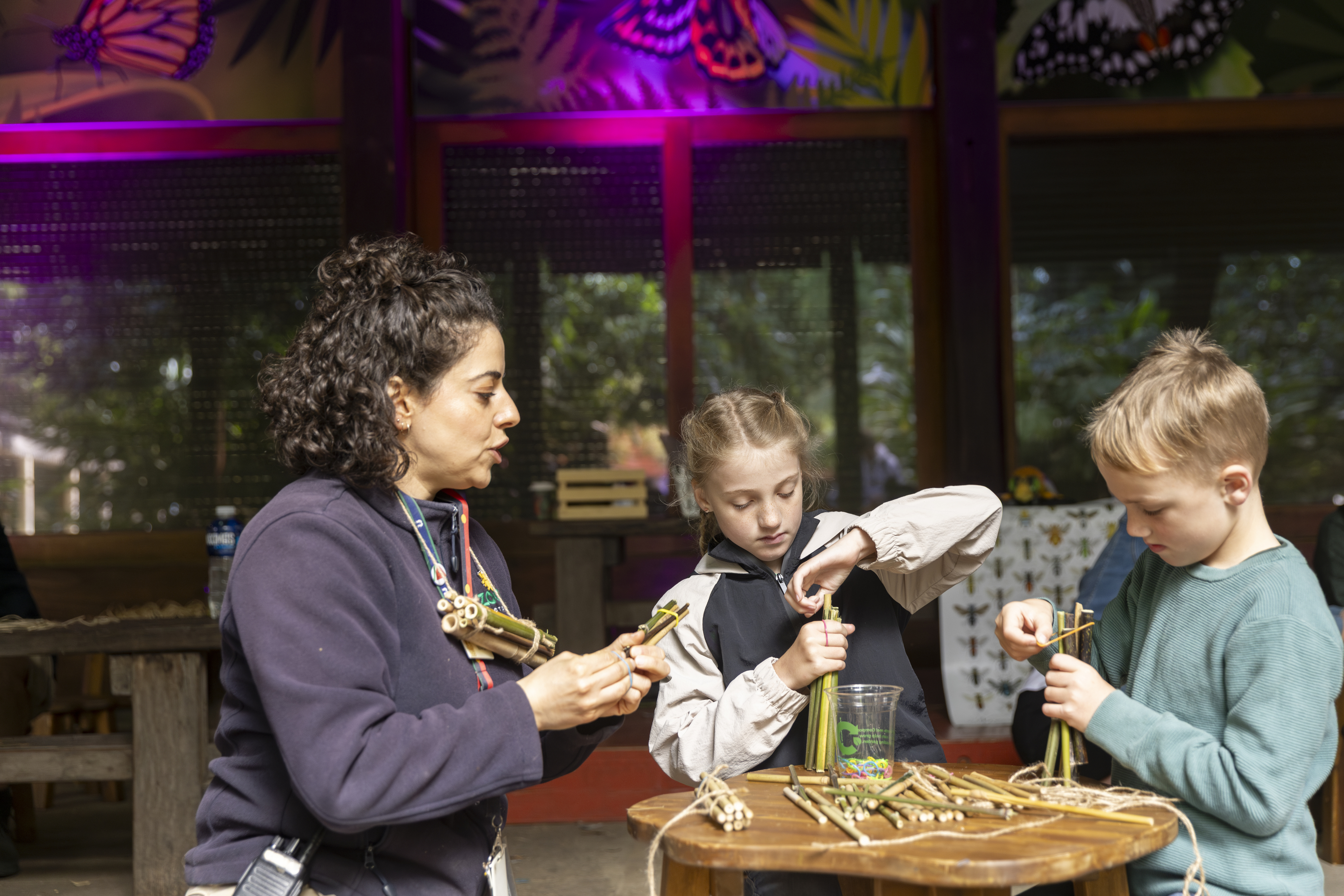 A volunteer and two young guests creating Bee-themed crafts, at the Old Elephant Barn, set up as a "Bee Hotel."